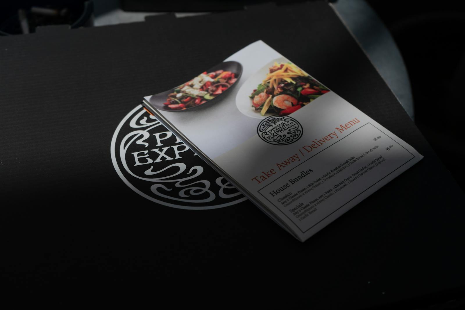 Close-up of a restaurant takeaway menu placed on a black surface, showcasing vibrant food imagery.