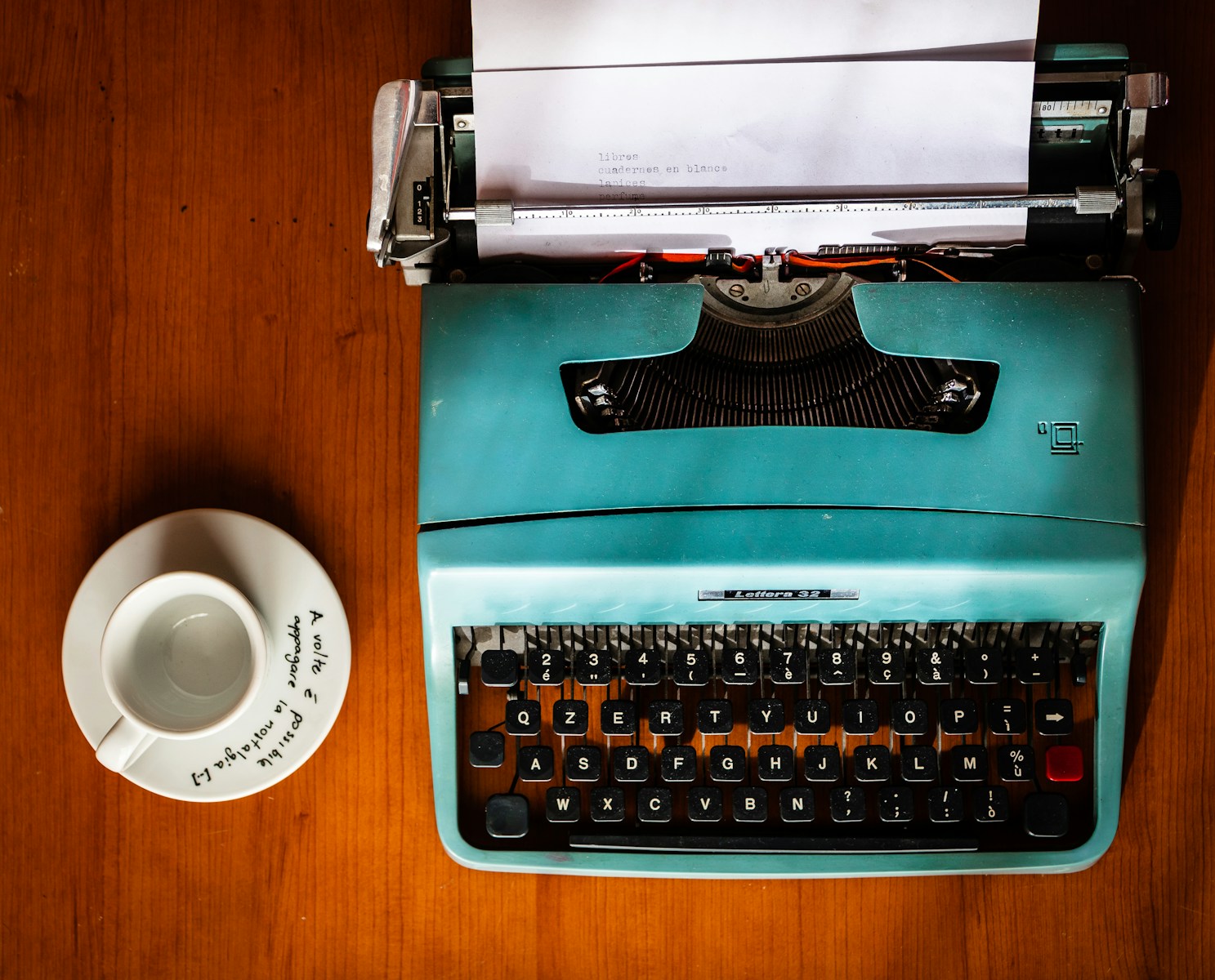 green and black typewriter beside white ceramic mug on brown wooden table