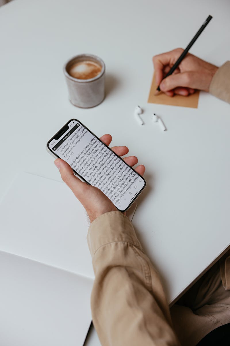 Close-up of a hand holding a smartphone while writing a note. Minimalistic indoor scene.